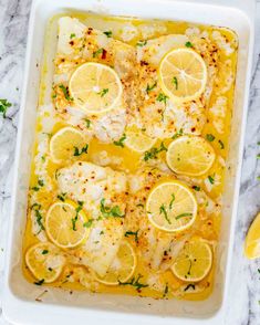 a casserole dish with lemons and chicken in it on a marble surface