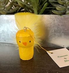 a yellow plastic toy with a tag attached to it sitting on a table next to a potted plant