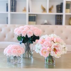 three vases filled with pink and white flowers on top of a table next to a couch