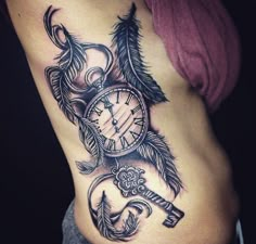 a woman's stomach with an arrow, clock and feathers tattoo on her side