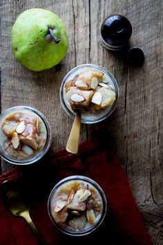 three glasses filled with dessert sitting on top of a wooden table next to an apple