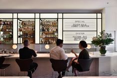 three people sitting at a bar with wine glasses in front of them and menus on the wall behind them