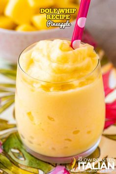 a close up of a drink in a glass with a straw on the top and pineapples behind it