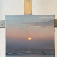 an easel with a painting on it that has a sunset over the ocean in the background