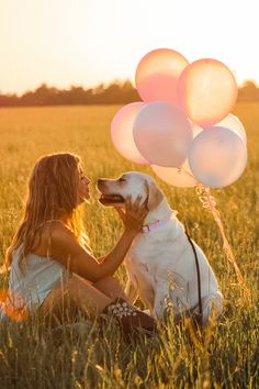 a woman sitting in the grass with her dog and balloons