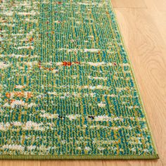 a green rug with white and red flowers on it sitting on a wooden floor next to a hardwood floor