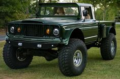 a large green truck parked on top of a lush green grass covered field next to trees