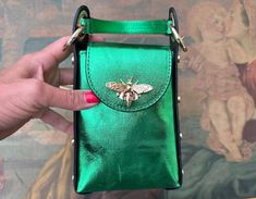 a hand holding a green purse with a bee on it's front and side