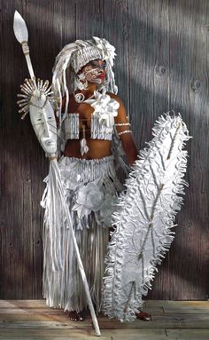 a woman dressed in white with feathers and holding a spear standing next to a wooden wall