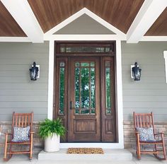 two rocking chairs on the front porch of a house with an entry door and potted plant