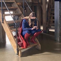 a woman in a superman costume sitting on a wooden chair looking at her cell phone