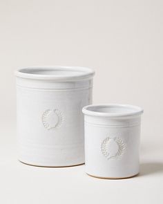 two white ceramic containers sitting next to each other on a white surface with no one around them