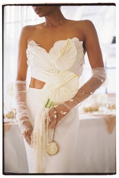 a woman in a white wedding dress holding a flower and a coin on her arm