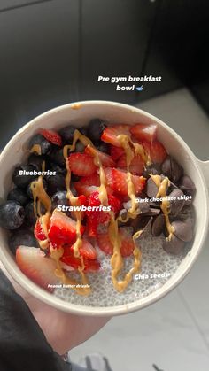 a bowl filled with fruit and nuts on top of a white counter next to a person's hand