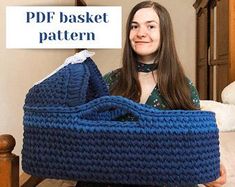 a woman sitting on the floor holding up a blue knitted basket