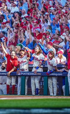 some baseball players are standing in the dugout with their hands up and fans behind them