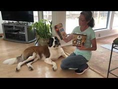 a woman sitting on the floor reading a book to her dog