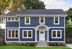 a blue two story house with white trim on the front door and windows, along with green grass