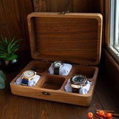 an open wooden box with four watches in it on a table next to a potted plant