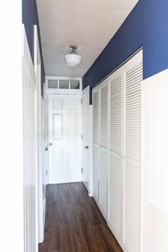 an empty hallway with white doors and blue accent paint on the walls, along with wood flooring