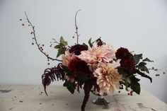 a vase filled with lots of flowers on top of a wooden table next to a white wall