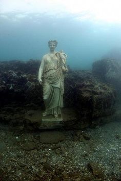 a statue is underwater in the ocean with rocks and gravel around it, as well as water