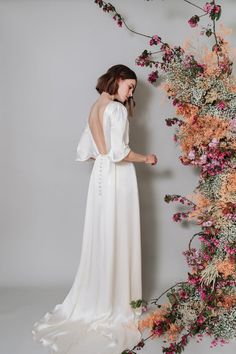 a woman in a white dress standing next to an arrangement of pink and orange flowers