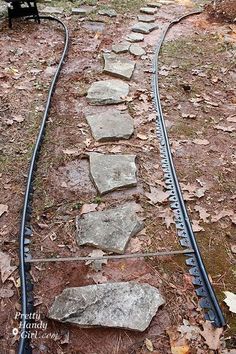 a set of train tracks in the woods with rocks on one side and a bench at the end