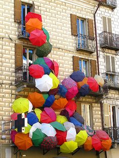 many colorful umbrellas are hanging from the side of a building in front of balconies