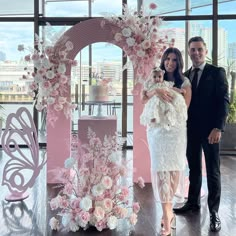 a man and woman standing next to each other in front of a pink floral arch