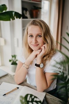 a woman sitting at a desk with her hand on her chin and looking into the camera