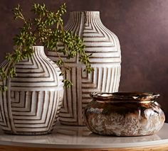 three white vases sitting on top of a table next to a potted plant