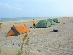 two tents pitched up on the beach next to each other with one person standing in front of them