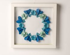 an origami wreath made out of blue and green paper in a white frame