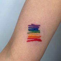 a rainbow colored crayon stick tattoo on the arm