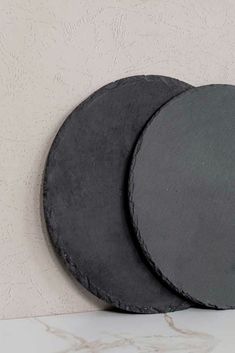 two black plates sitting next to each other on a white counter top with a wall in the background