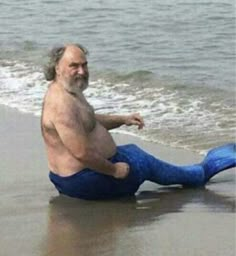 an older man sitting on the beach with his legs spread out and feet in the water