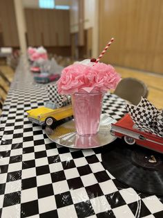 a pink flower in a vase sitting on top of a table next to an old car