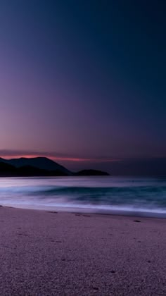 the sun is setting over the ocean with mountains in the distance and waves crashing on the beach