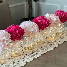 pink and white hydrangeas are lined up on a lace tablecloth with mason jars