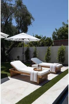 two chaise lounge chairs and an umbrella in a backyard