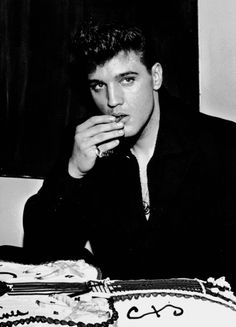 a man sitting at a table with a cake in front of him and his hand to his mouth