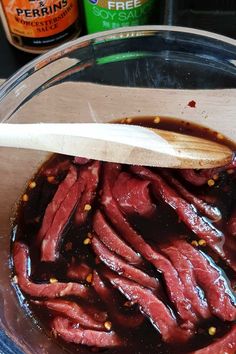 a wooden spoon is in a bowl full of meat and sauce on the table next to some bottles