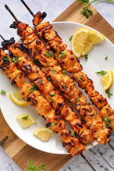 grilled chicken skewers on a white plate with lemon wedges and parsley