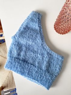 a blue knitted top next to two different colored pieces of yarn on a white surface