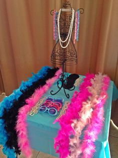 a table topped with pink and blue feathers next to a mannequin wearing a necklace