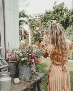 a woman is arranging flowers in buckets on a table outside the house and looking at them