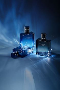 two bottles of perfume sitting next to each other on a blue and white background with lights