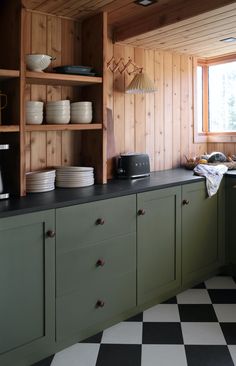 a kitchen with black and white checkered flooring, green cabinets and open shelving