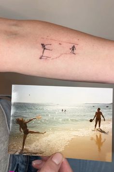 a person with a small tattoo on their arm holding up a photo of two people playing in the water